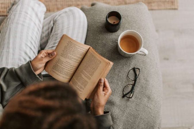 Vue d'en haut d'une personne lisant un vieux livre, créant un coin lecture parfait avec une boisson chaude et des lunettes.