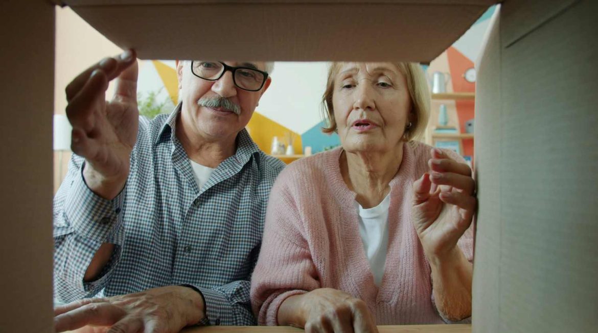 Un couple de seniors ouvrant un carton de déménagement, idéal pour illustrer une demande d'aide financière au déménagement pour les retraités et personnes âgées.