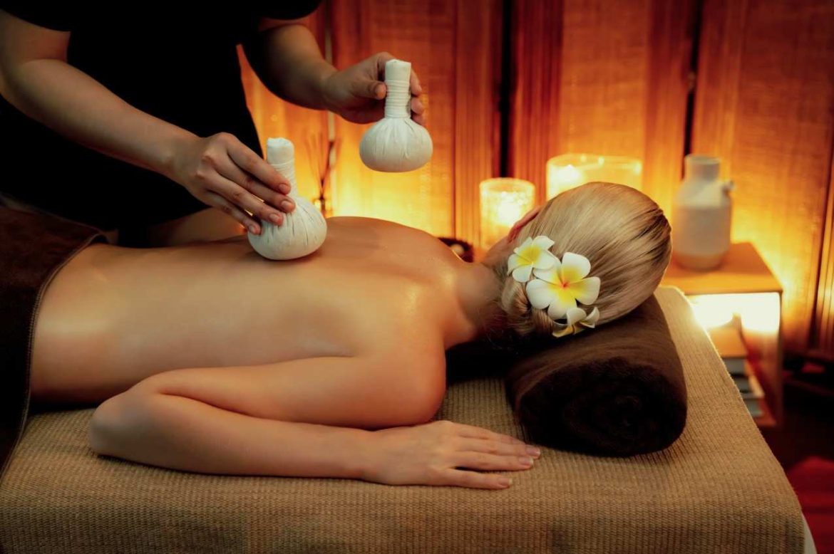 Praticienne appliquant un massage aux tampons de plantes chauds sur le dos d'une femme allongée dans un spa.