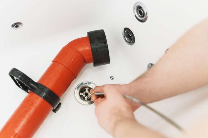 Un technicien visse la bonde reliée au mécanisme de vidage d'une baignoire.